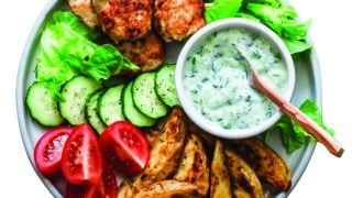 Fish skewers, baked potatoes, vegetables and yogurt greens sauce on dark background, top view